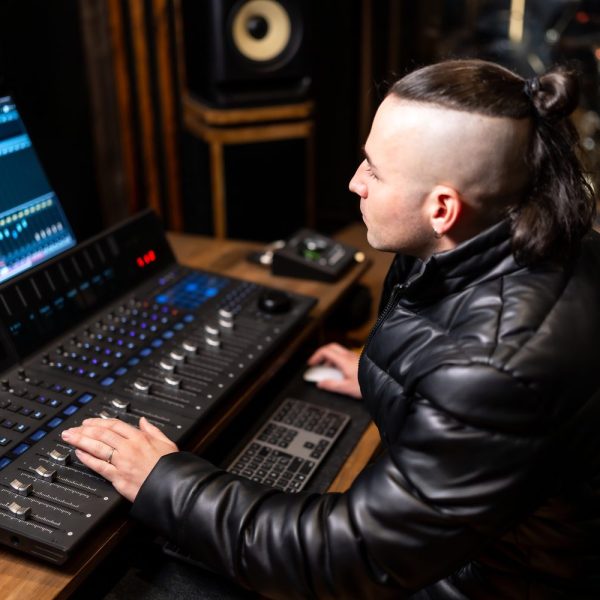 Producteur de musique ajustant une ligne de basse 808 sur un logiciel audio, devant des moniteurs de studio.