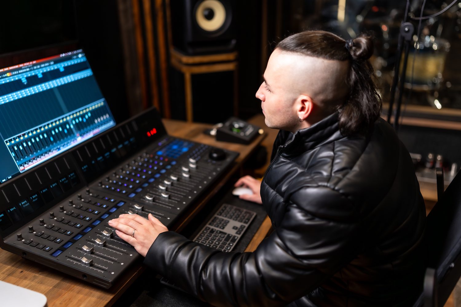 Producteur de musique ajustant une ligne de basse 808 sur un logiciel audio, devant des moniteurs de studio.