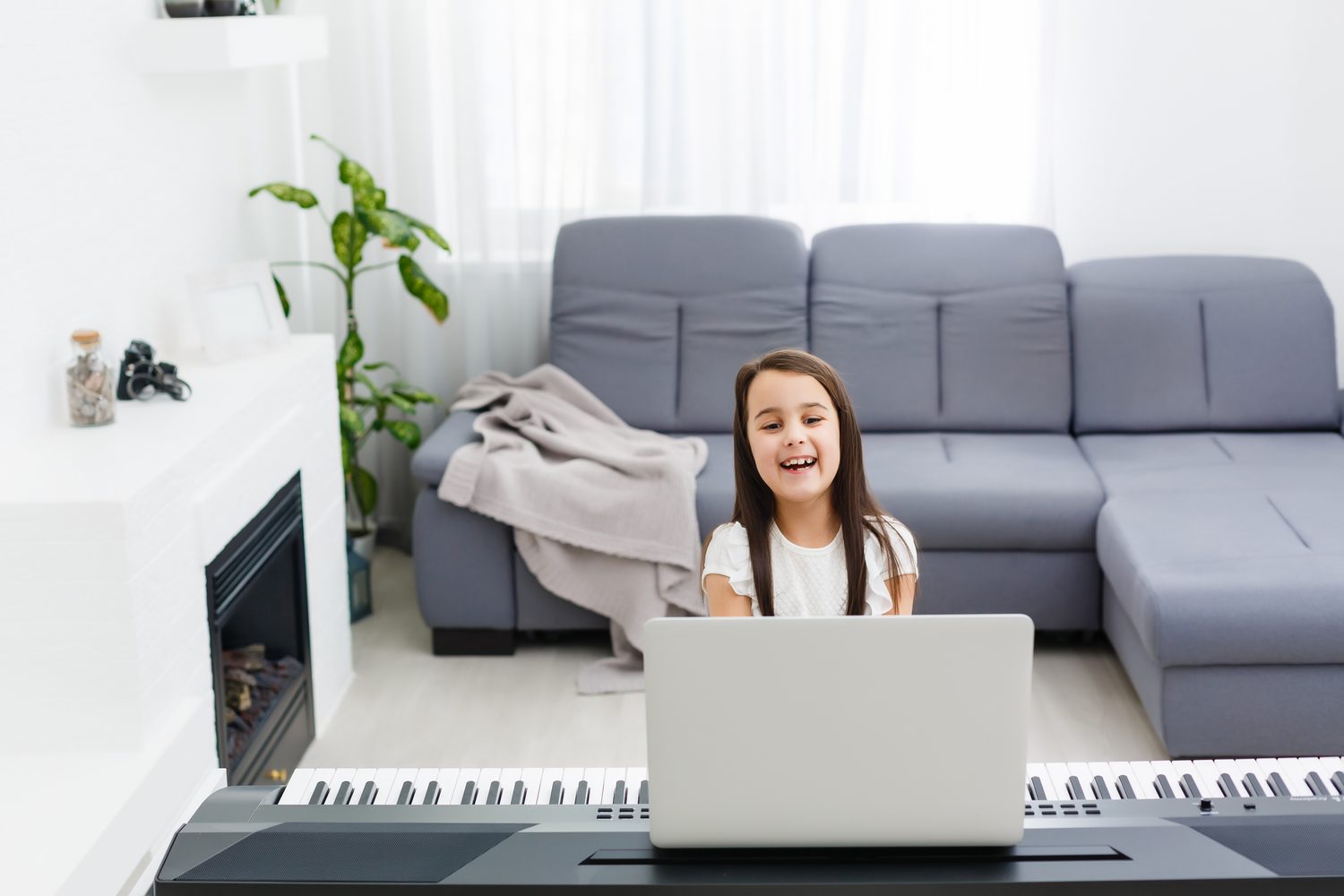 Un piano numérique compact installé dans un petit salon, près d’un canapé et d’une fenêtre.